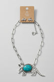 A silver-toned paperclip chain necklace with an armadillo pendant featuring a turquoise stone, displayed on a brown cardboard hanger against a textured beige background.